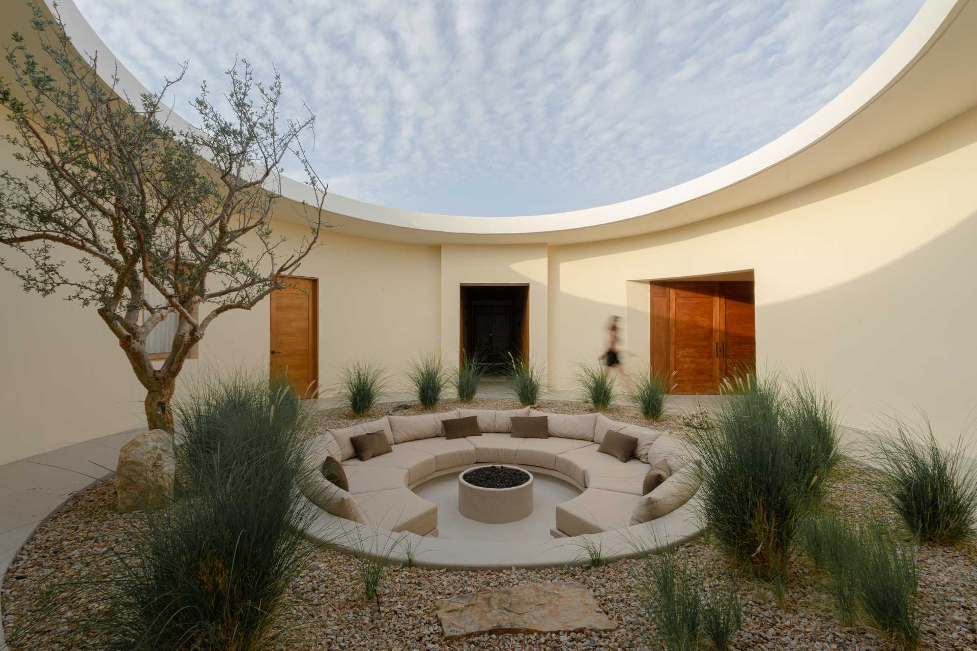 A contemporary house has an internal courtyard, at the center of this circular space lies a fire pit, surrounded by a sunken circular sofa that invites gathering and contemplation.