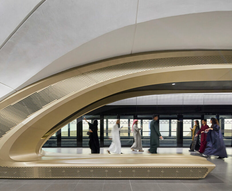 People walking in modern, futuristic train station with curved architectural design.