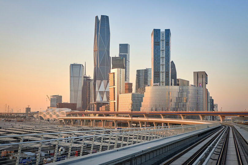 Skyline of a modern city with tall skyscrapers and a railway in the foreground under a clear sky.
