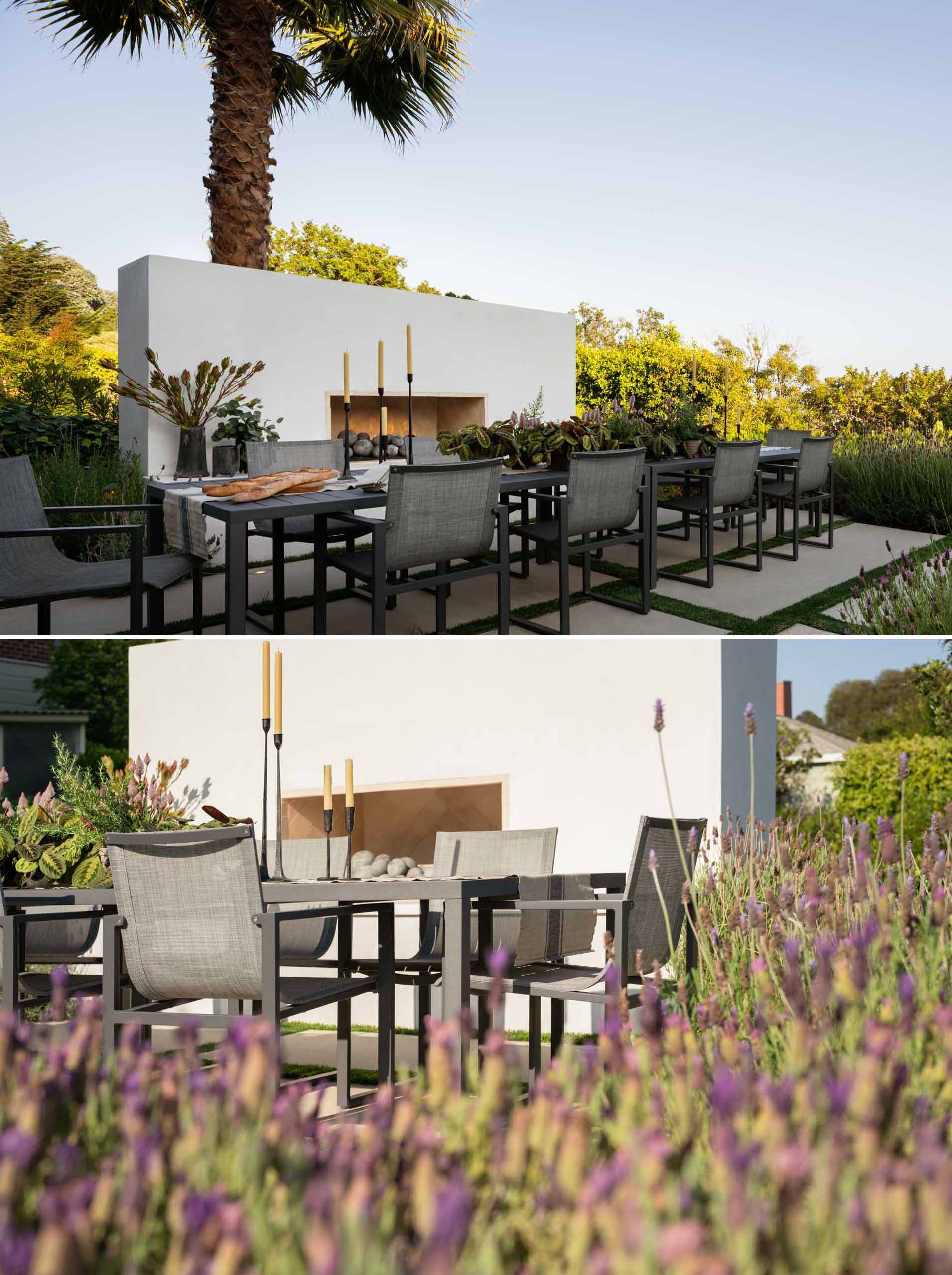 This contemporary outdoor dining space features a striking rectangular table with minimalist chairs, creating a clean and inviting setting for alfresco dining. Surrounded by carefully arranged greenery, including lavender, and clean stone pavers, the design emphasizes simplicity and elegance. Subtle lighting and a fireplace enhances the space, making it ideal for both daytime meals and evening gatherings, blending modern aesthetics with nature’s tranquility.