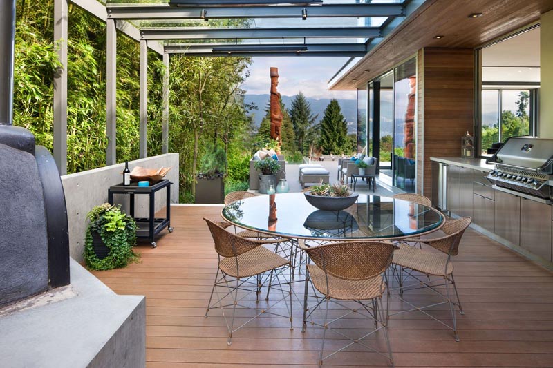 This modern outdoor dining space features a sleek glass-topped dining table set against a backdrop of minimalist design. With a built-in BBQ and spacious countertops for meal prep, it’s a perfect blend of style and functionality. The space is elevated by clean lines, comfortable seating, and thoughtful details that make it an ideal spot for both cooking and entertaining.