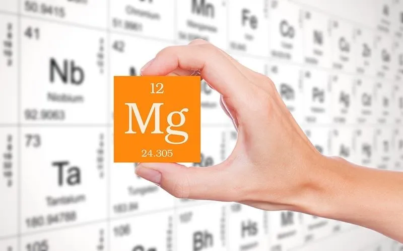 Hand holding a magnesium illustration against a periodic table background.