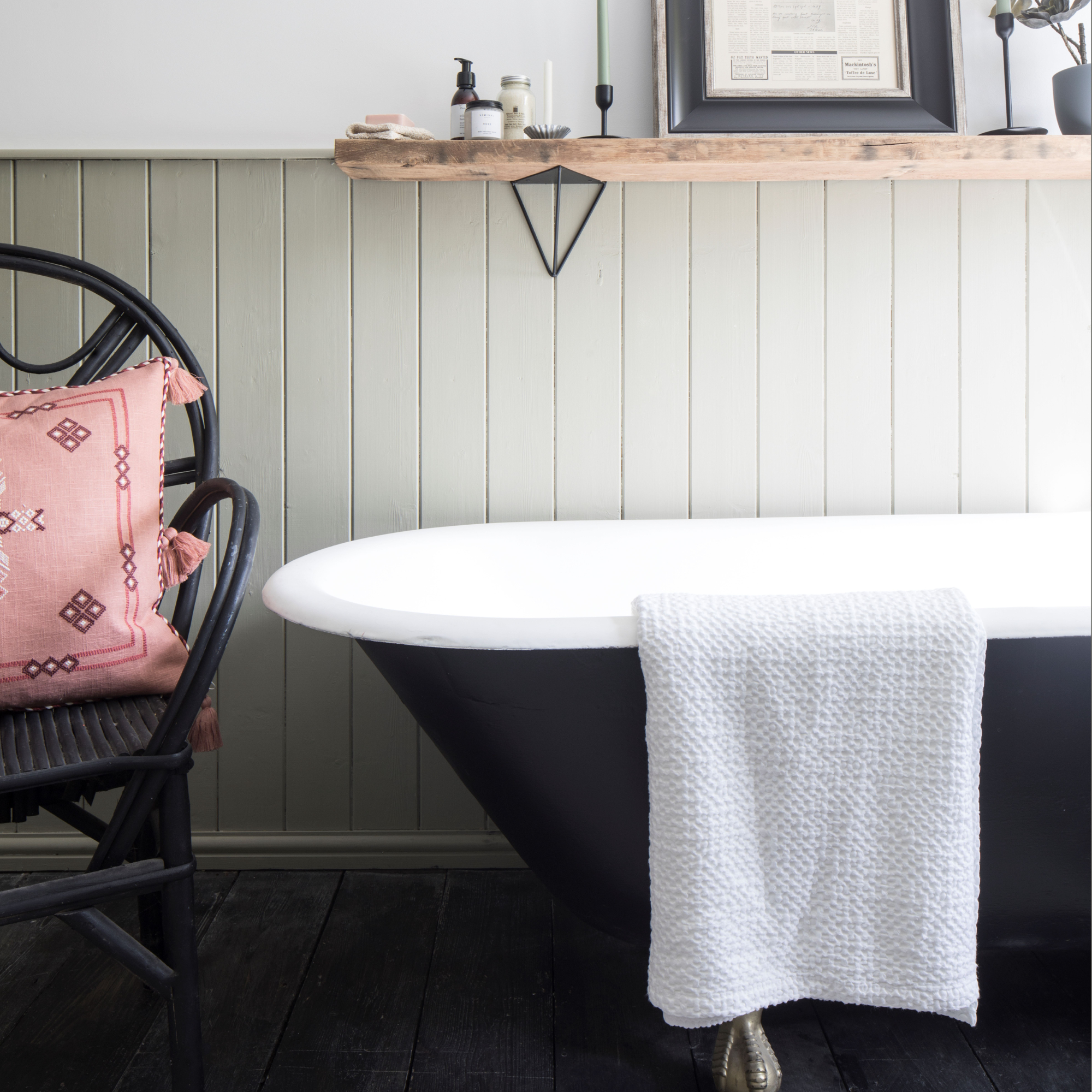 White bath towel hanging on edge of black bathtub in panelled bathroom
