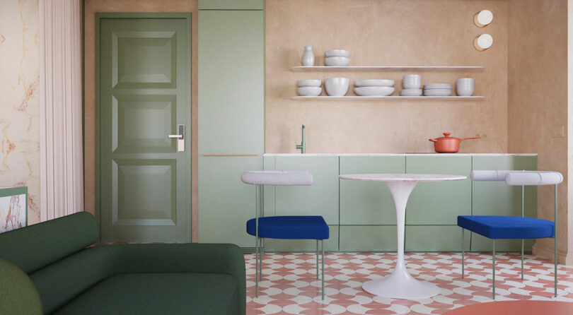 Modern kitchen with sage green cabinets, open shelves, round white table, two blue-cushioned chairs, green sofa, and patterned tile floor. Red pot sits on the counter.