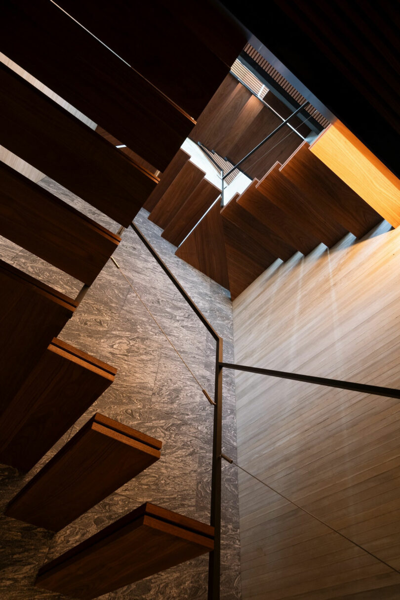 Floating wooden stairs attached to a wall with natural light streaming in from above, highlighting the geometric design and textured surfaces.