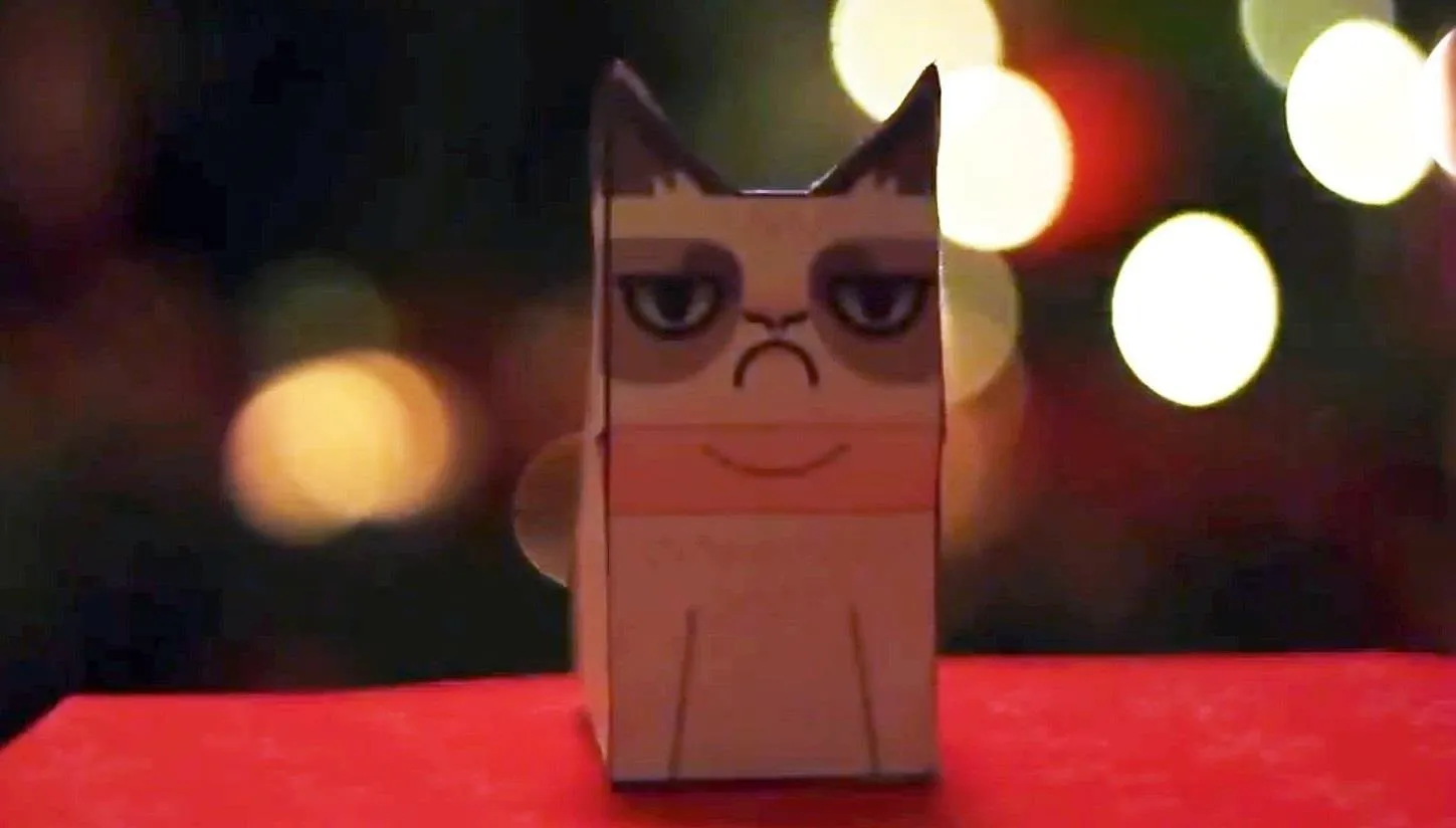 Grumpy cat paper figurine in front of colorful bokeh lights.