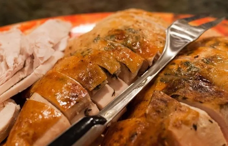 Sliced roasted turkey on a plate with a carving fork.