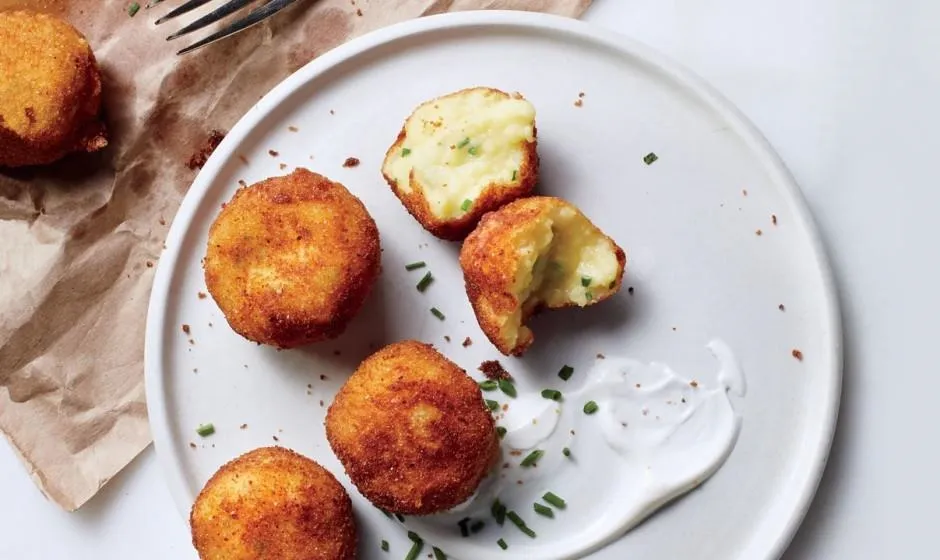 Crispy potato balls on a white plate with dipping sauce.