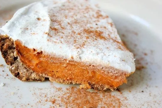 Slice of pumpkin pie topped with whipped cream and sprinkled with cinnamon.