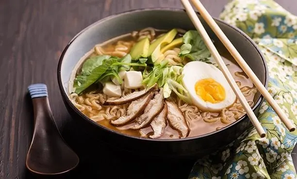 Bowl of ramen with vegetables, egg, and sliced meat, served with chopsticks.
