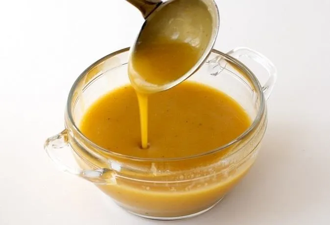 Rich golden soup being poured from a ladle into a glass bowl.