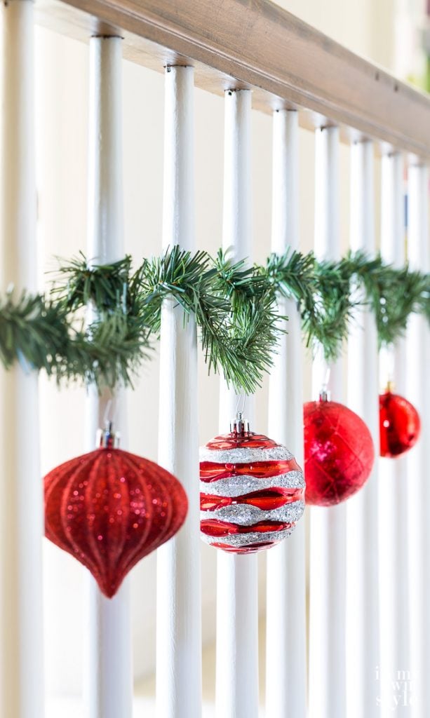 Christmas ornaments hung on staircase spindles with garland ties.
