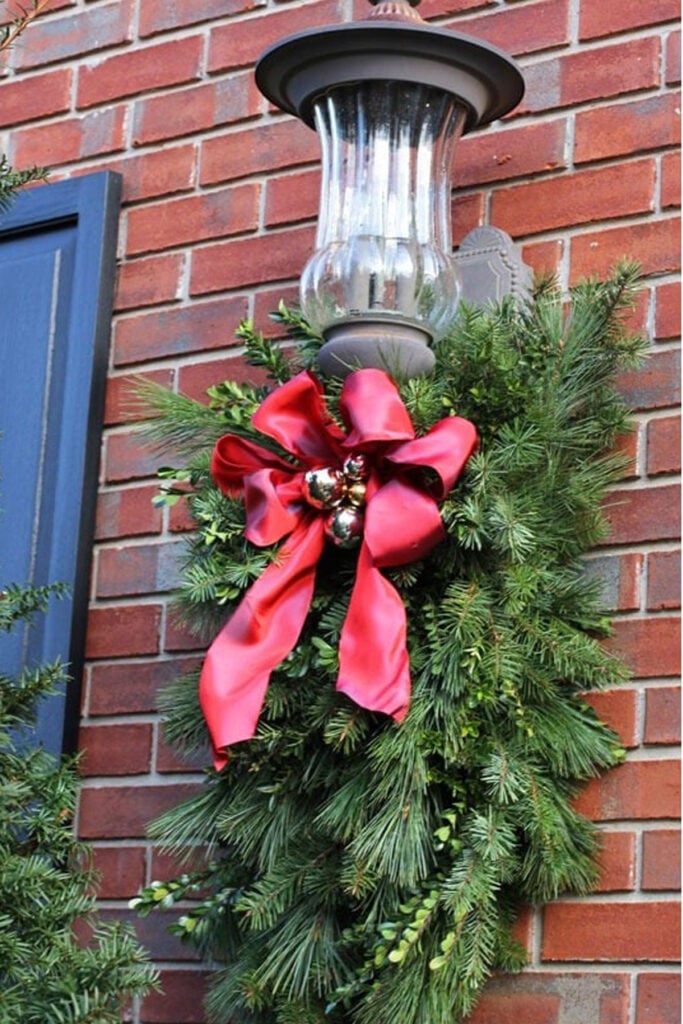 Christmas-Outdoor-Greenery- Large front porch light decorated for Christmas using a clever DIY trick to hang greenery and attach ribbon.