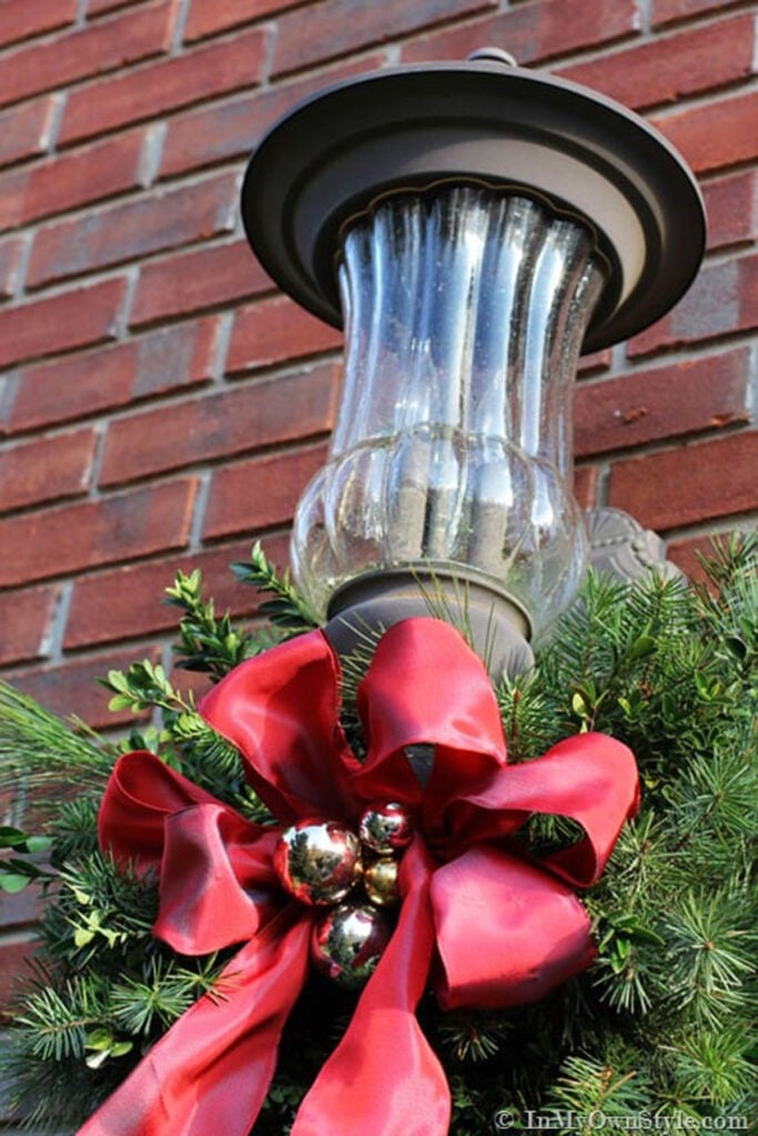 Outdoor-Holiday-Decorating close up of an exterior front porch light decorated for Christmas using real greenery and red ribbon.