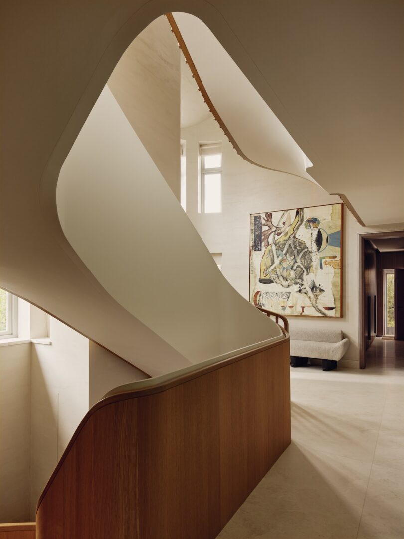 Modern interior with a curved staircase featuring wooden accents, large abstract artwork on the wall, neutral-colored floors, and natural light from tall windows.