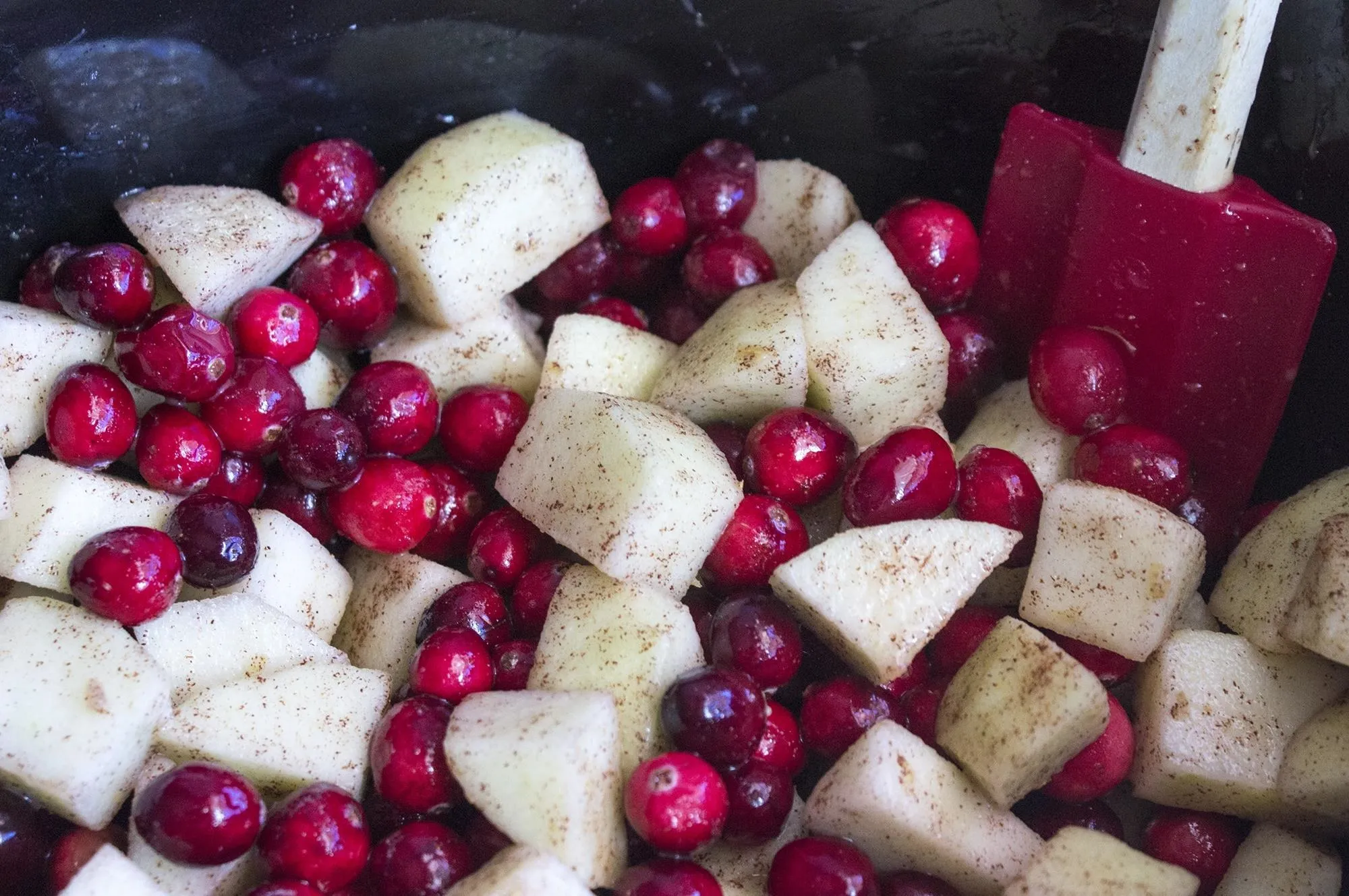 Cranberries and diced apples in a bowl with a red spatula.