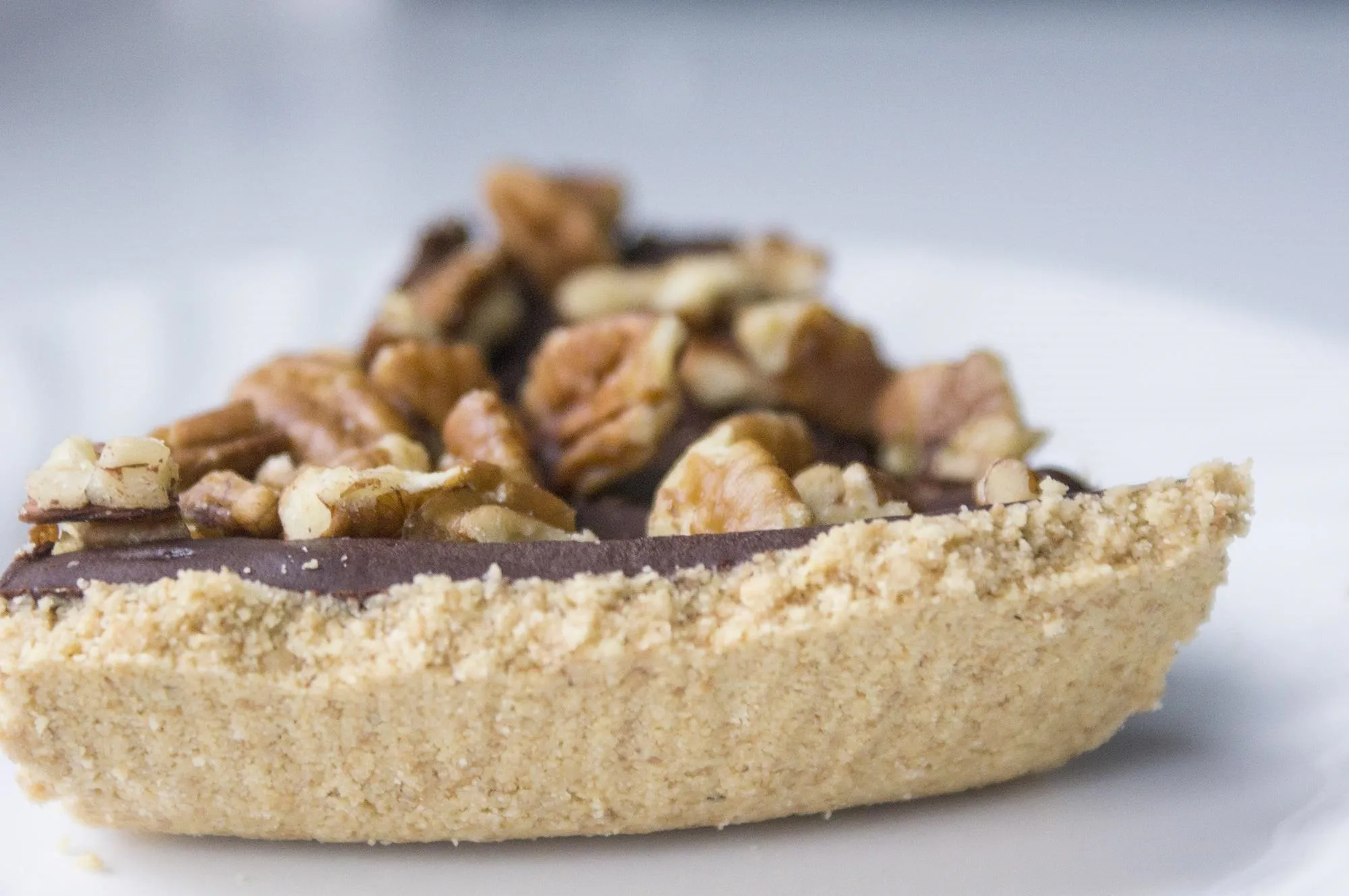 Chocolate tart topped with chopped nuts on a white plate.